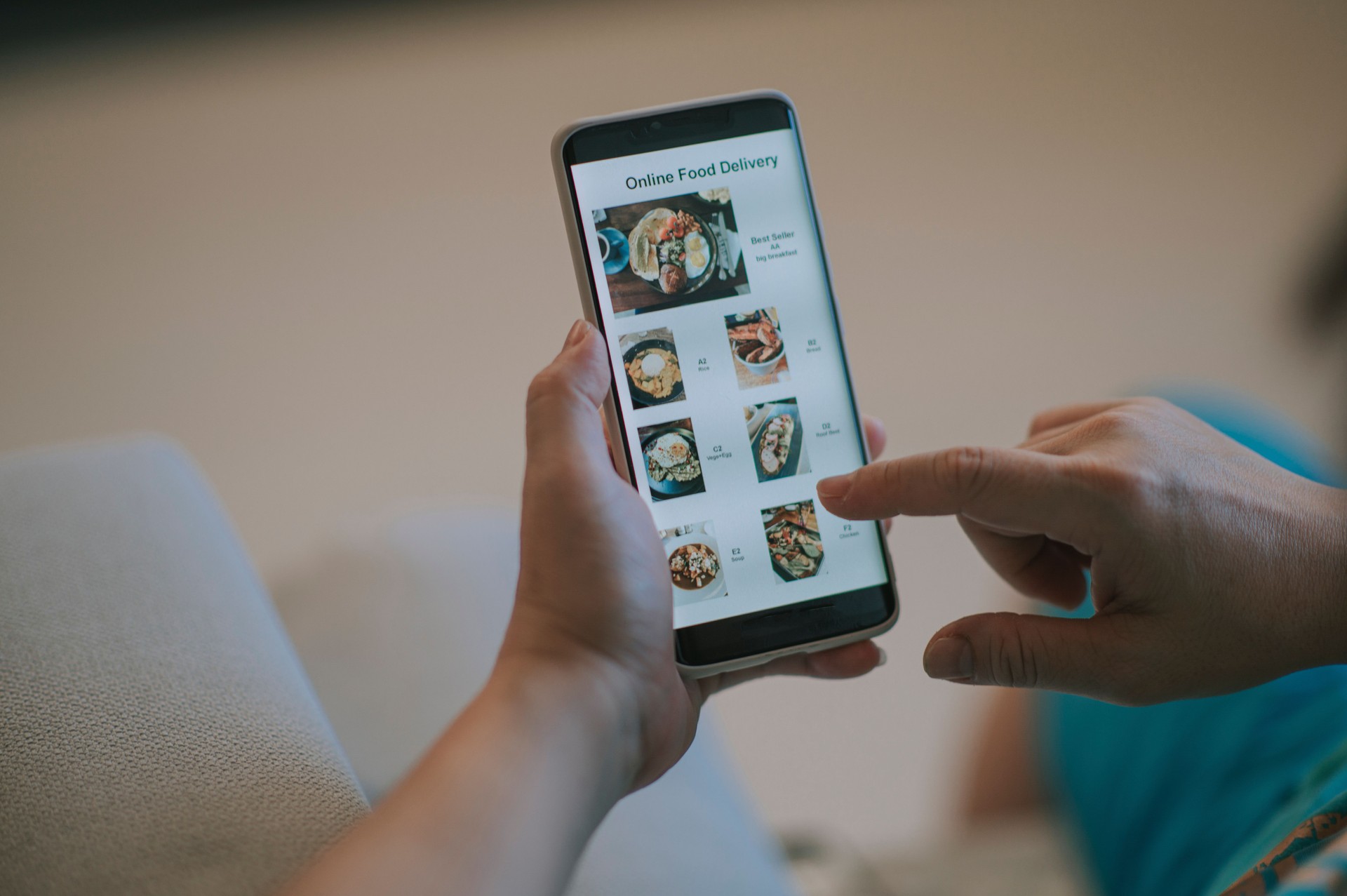 Online food delivery mobile app shown on smart phone screen hold by asian woman hands in living room